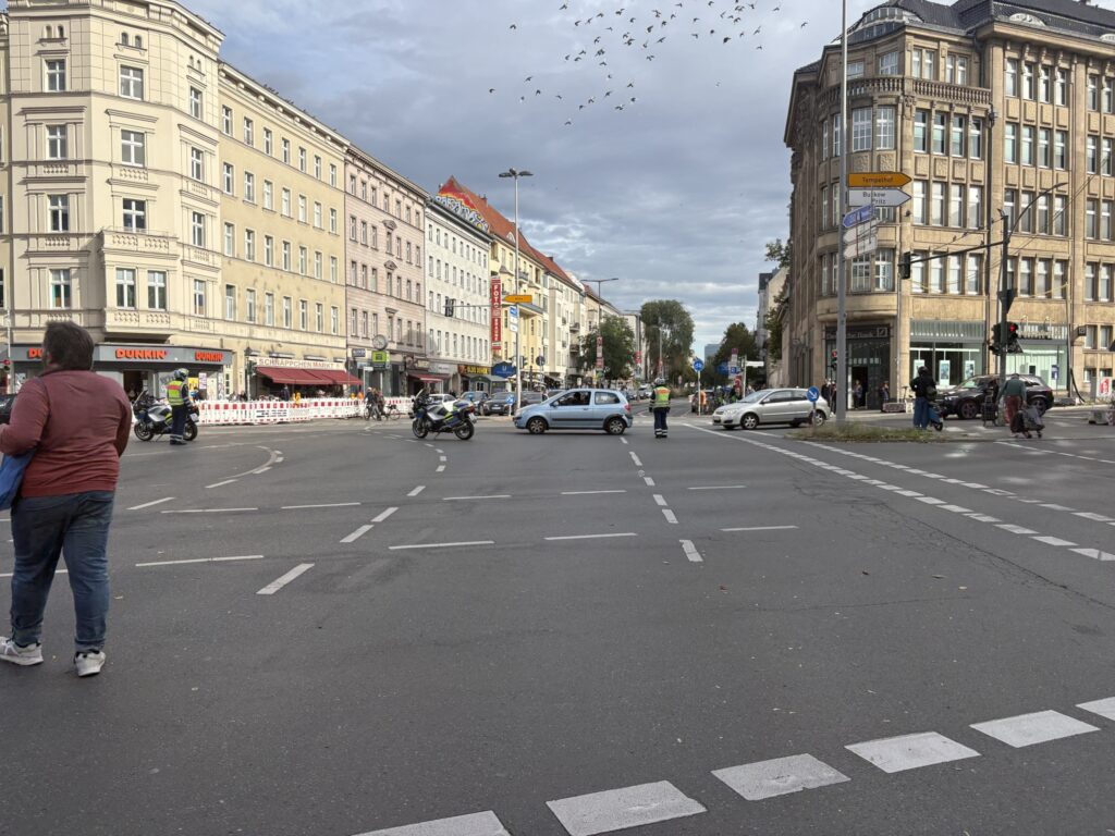 Absperrung der Polizei durch eine Person und ein Motorrad. An diesen fahren Autos vorbei.
